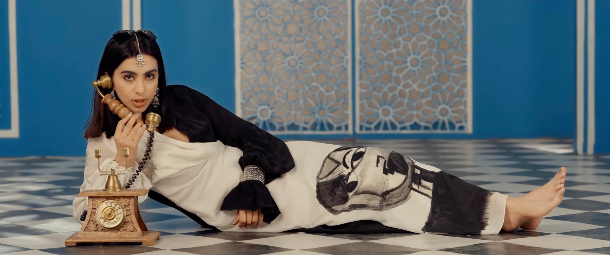 Ranjani reclining on a checkerboard floor, holding a vintage brass telephone