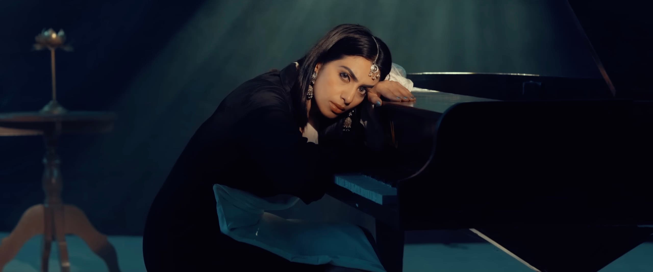 Ranjani leaning on a grand piano under a teal spotlight